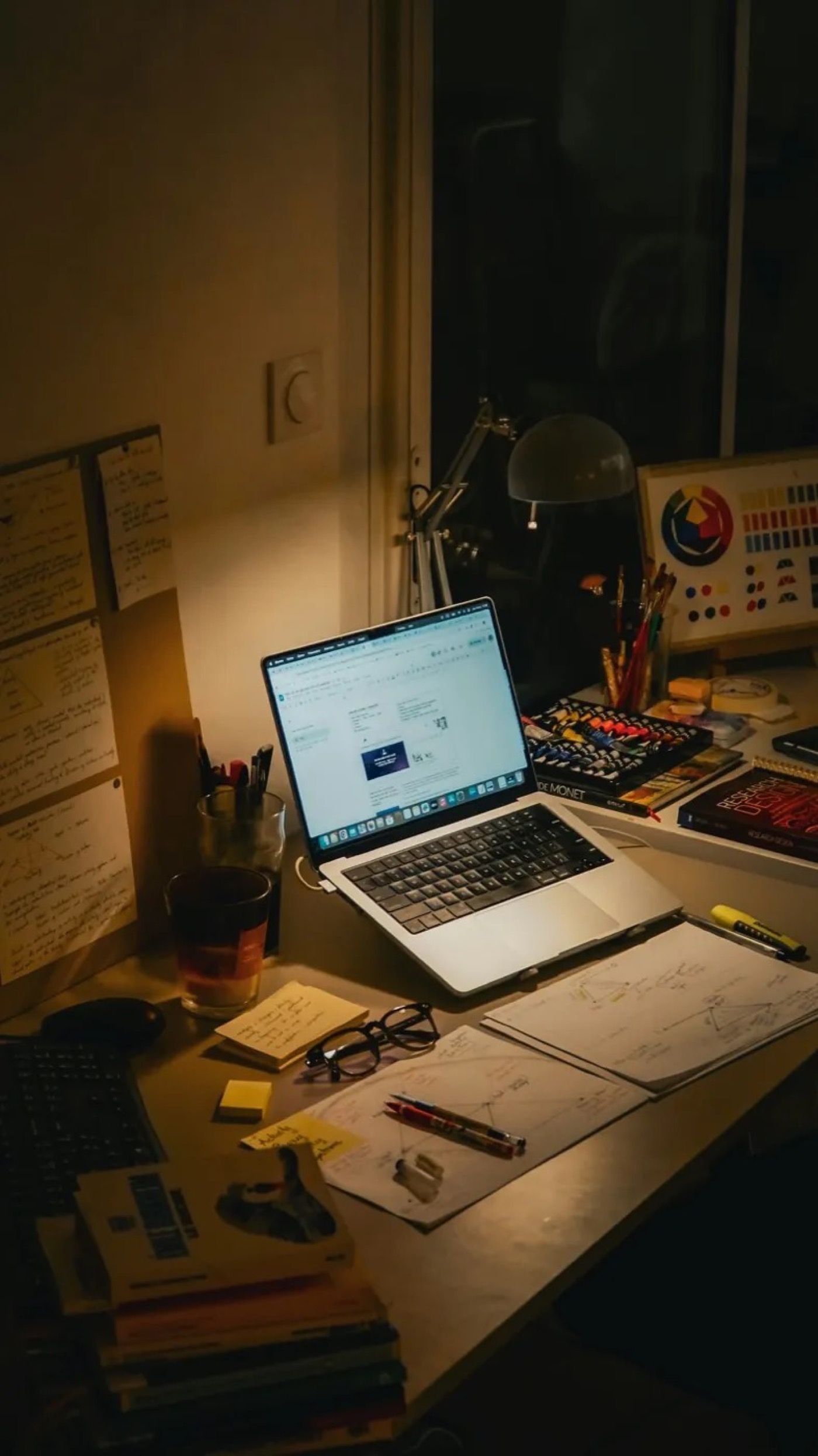 A cluttered desk with paperwork late in the evening